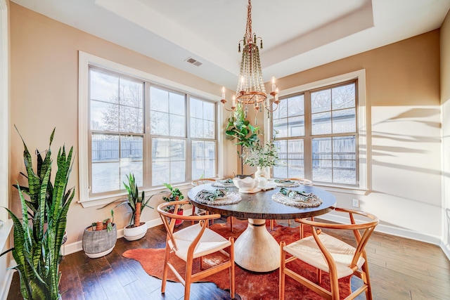 dining room featuring visible vents, baseboards, hardwood / wood-style flooring, a tray ceiling, and a notable chandelier