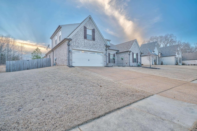 view of front facade featuring driveway, an attached garage, fence, and brick siding