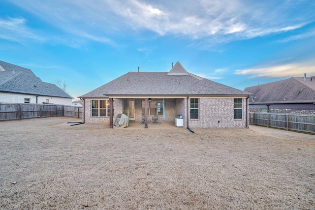 back of house featuring a patio, brick siding, roof with shingles, and a fenced backyard