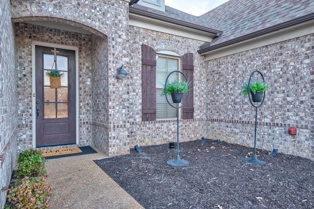 entrance to property with a shingled roof and brick siding