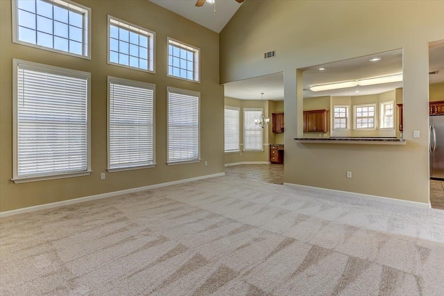 unfurnished living room with carpet floors, high vaulted ceiling, baseboards, and ceiling fan with notable chandelier