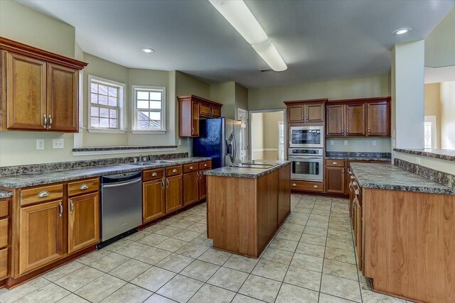 kitchen with light tile patterned floors, a sink, a kitchen island, appliances with stainless steel finishes, and dark countertops