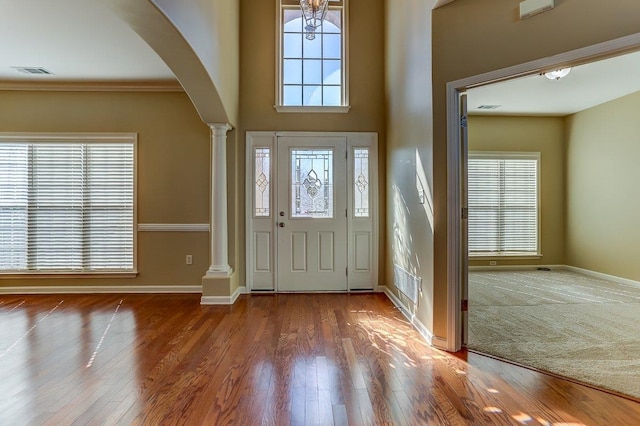 entrance foyer featuring baseboards, visible vents, arched walkways, wood finished floors, and ornate columns