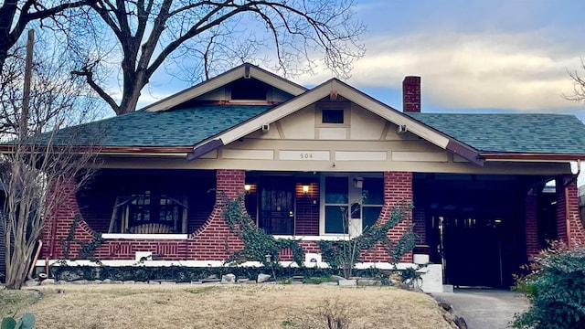 view of front of home with brick siding, a chimney, and a shingled roof