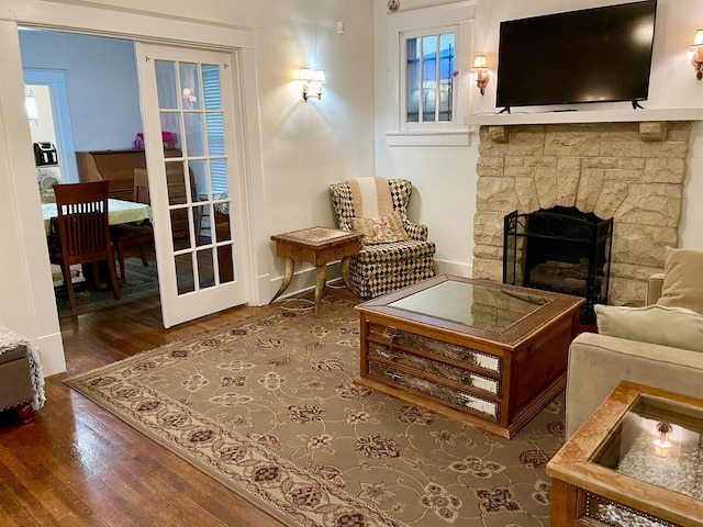 living area featuring a stone fireplace, baseboards, and wood finished floors