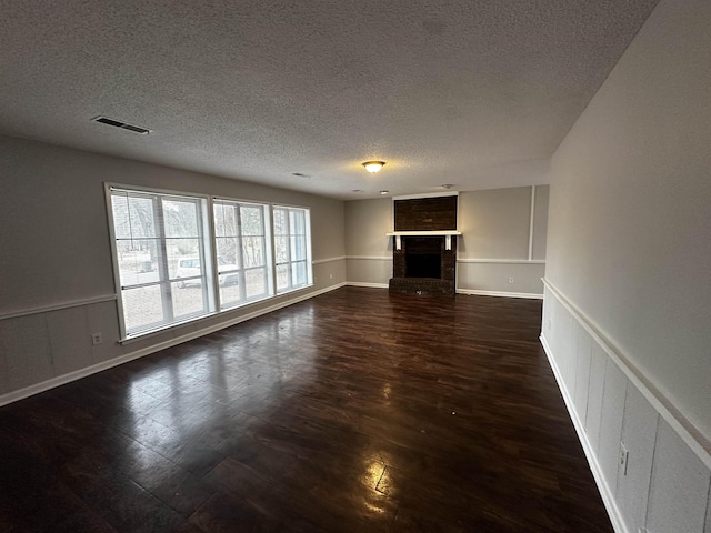 unfurnished living room featuring a textured ceiling, a wainscoted wall, a fireplace, visible vents, and dark wood finished floors