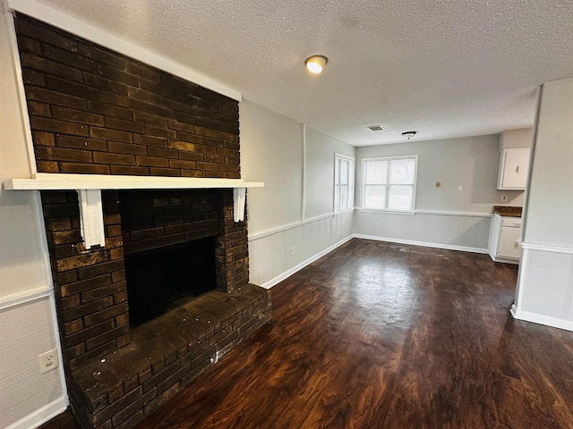 unfurnished living room with a textured ceiling, wainscoting, dark wood-style flooring, and a fireplace