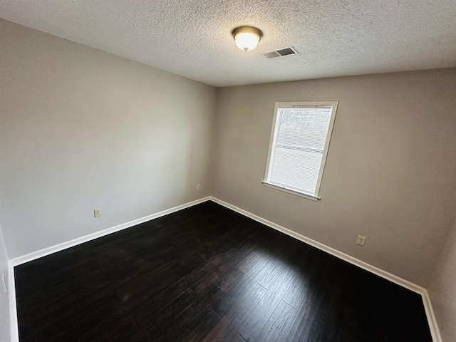 empty room featuring dark wood-type flooring, visible vents, a textured ceiling, and baseboards