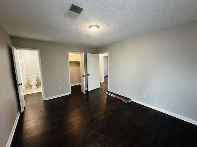 unfurnished bedroom with a walk in closet, dark wood finished floors, visible vents, connected bathroom, and baseboards