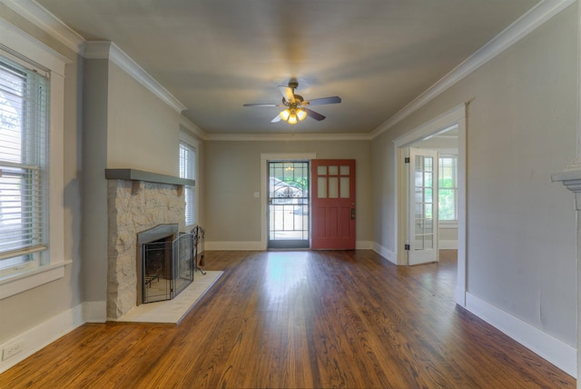 unfurnished living room featuring a wealth of natural light, crown molding, wood finished floors, and a stone fireplace