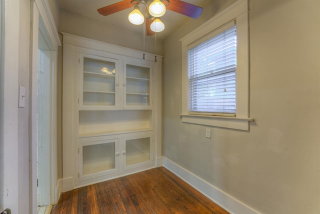 unfurnished dining area featuring ceiling fan, built in shelves, baseboards, and dark wood-style flooring