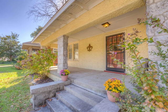 property entrance featuring covered porch, a yard, and stucco siding