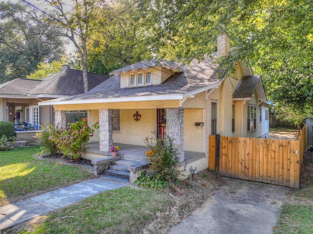 view of front of house with stucco siding, a chimney, fence, a porch, and a front yard