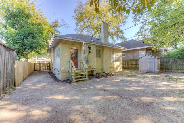 rear view of house featuring a chimney, a gate, a storage unit, fence, and an outdoor structure