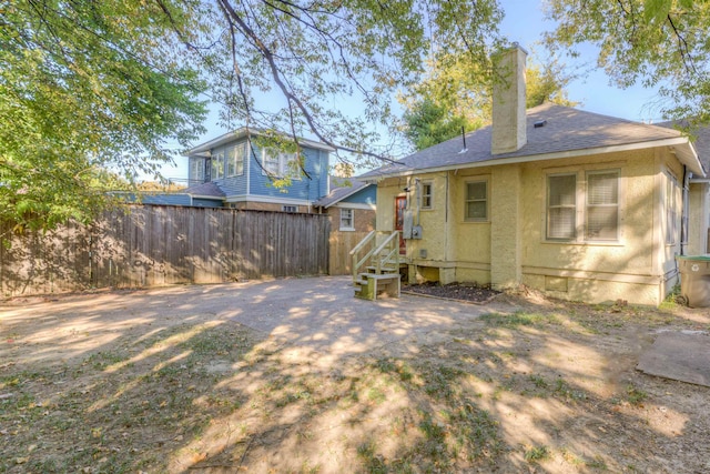 back of house with roof with shingles, a chimney, fence, and stucco siding