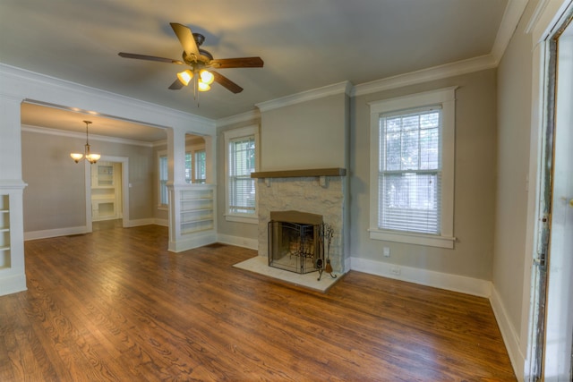 unfurnished living room with ceiling fan with notable chandelier, a stone fireplace, wood finished floors, and baseboards