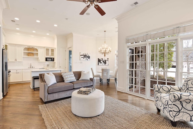 living area with visible vents, ornamental molding, wood finished floors, ceiling fan with notable chandelier, and recessed lighting