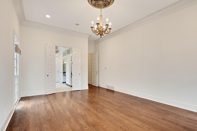 spare room featuring visible vents, an inviting chandelier, ornamental molding, wood finished floors, and baseboards