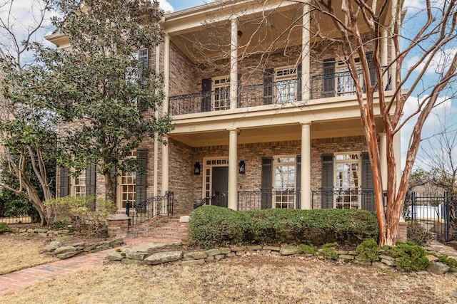 view of front facade featuring brick siding, a porch, fence, and a balcony