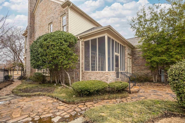 view of side of home featuring brick siding, fence, and a sunroom