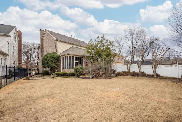 view of side of property with brick siding, a lawn, and a fenced backyard