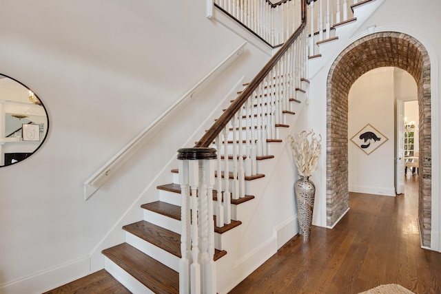 stairway with arched walkways, wood-type flooring, visible vents, a towering ceiling, and baseboards