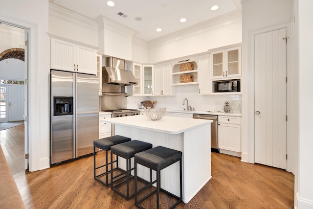 kitchen featuring stainless steel appliances, white cabinetry, light wood-style flooring, and wall chimney range hood