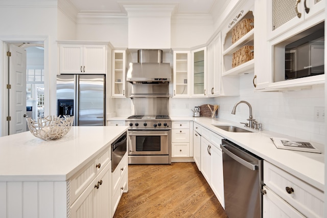 kitchen featuring wall chimney exhaust hood, light wood-style flooring, ornamental molding, stainless steel appliances, and a sink