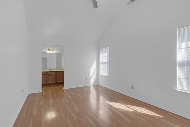 unfurnished living room featuring light wood-style floors, baseboards, high vaulted ceiling, and a ceiling fan