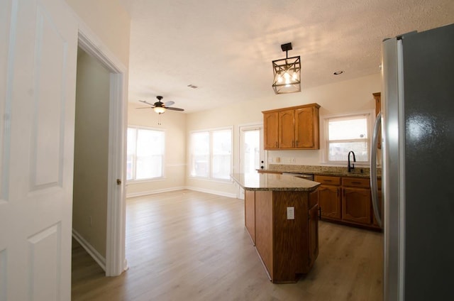 kitchen with light wood-style flooring, a sink, a kitchen island, freestanding refrigerator, and brown cabinets