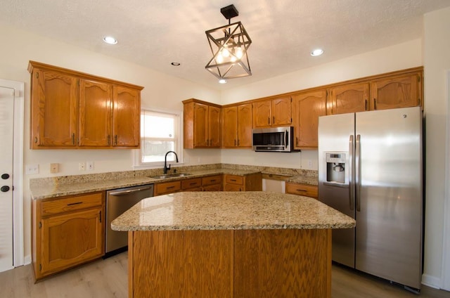 kitchen with appliances with stainless steel finishes, brown cabinetry, a sink, and light stone countertops