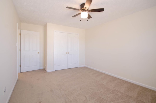 unfurnished bedroom featuring a closet, light carpet, a textured ceiling, and baseboards