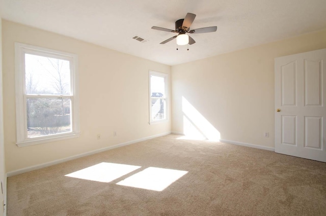 carpeted spare room featuring baseboards, visible vents, and ceiling fan