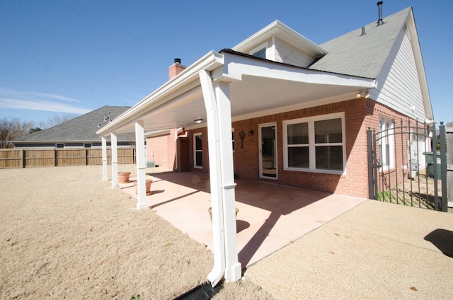 rear view of house featuring a patio area, brick siding, fence, and a chimney