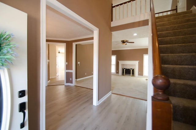 entrance foyer featuring crown molding, stairway, a tiled fireplace, light wood-style floors, and baseboards