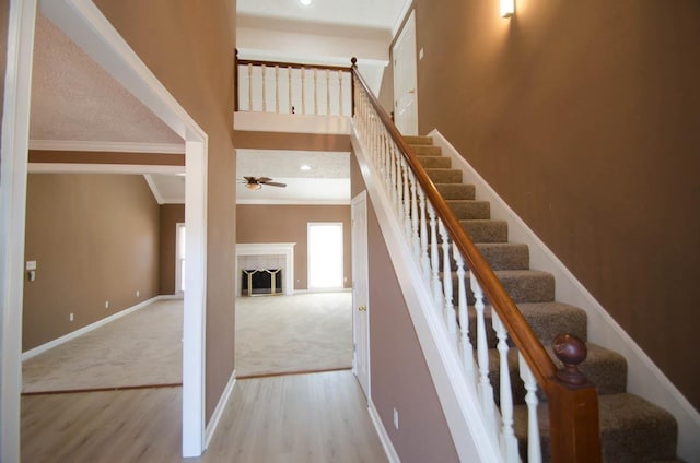 stairs with a fireplace, wood finished floors, a ceiling fan, baseboards, and ornamental molding