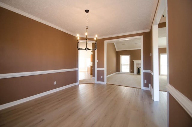 unfurnished dining area featuring baseboards, light wood-style flooring, ornamental molding, an inviting chandelier, and a fireplace