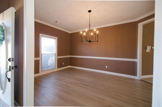 empty room with a textured ceiling, wood finished floors, baseboards, ornamental molding, and an inviting chandelier