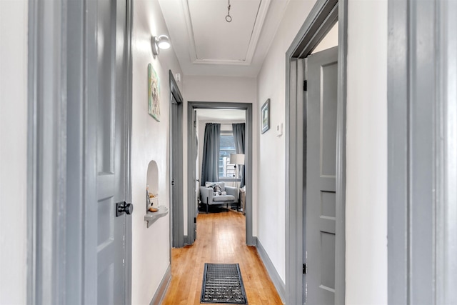 hallway with light wood-type flooring, attic access, and baseboards