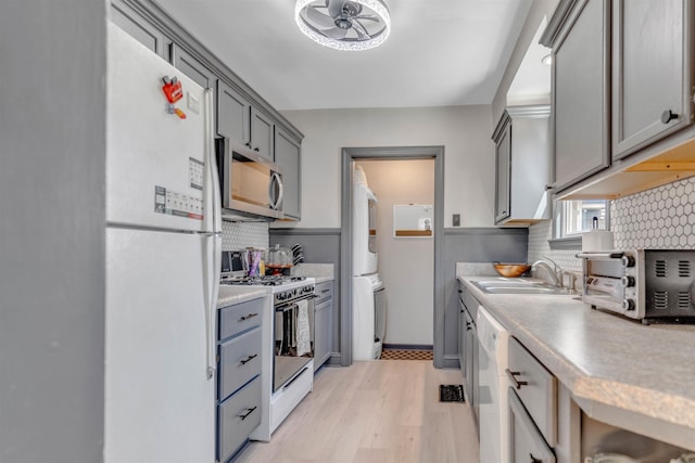 kitchen featuring white appliances, stacked washer / dryer, a sink, and gray cabinetry