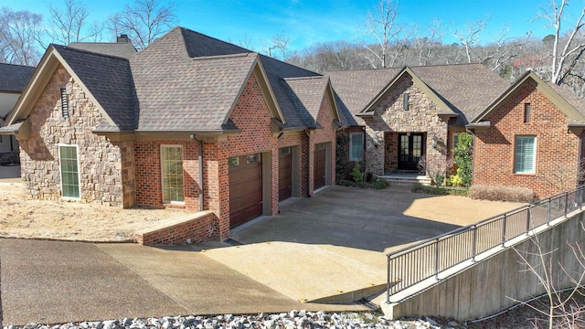 view of front of house featuring brick siding, a shingled roof, concrete driveway, a garage, and stone siding