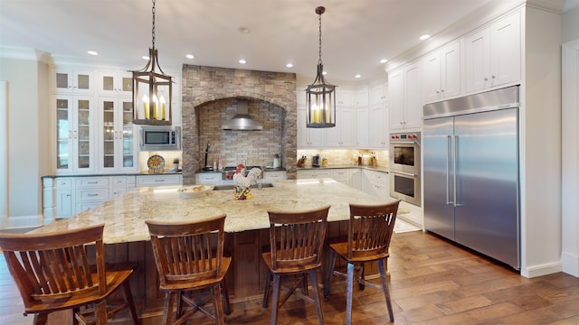 kitchen with built in appliances, dark wood-type flooring, white cabinetry, backsplash, and a large island with sink
