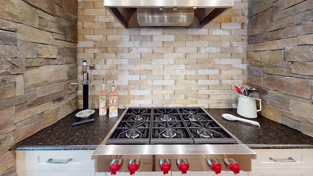 kitchen featuring wall chimney range hood, white cabinets, dark stone countertops, and gas range