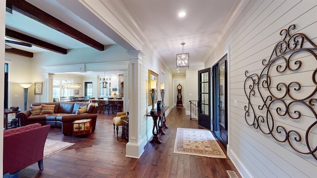 foyer entrance featuring beam ceiling, crown molding, a notable chandelier, dark wood-type flooring, and ornate columns