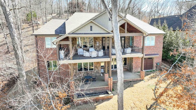 view of front of property with brick siding, a shingled roof, a patio area, a balcony, and stone siding