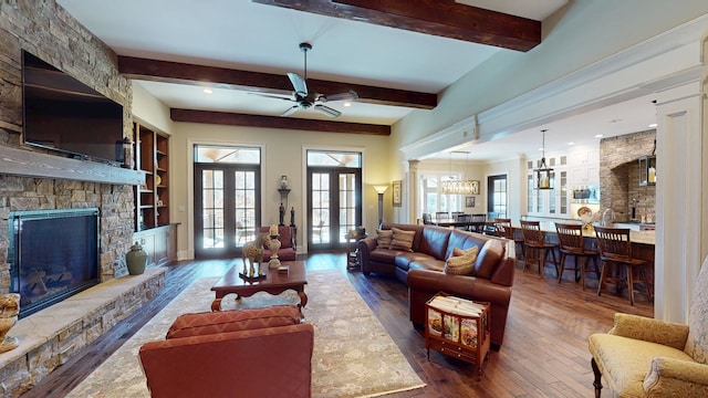living area with french doors, ceiling fan, hardwood / wood-style floors, a stone fireplace, and beam ceiling