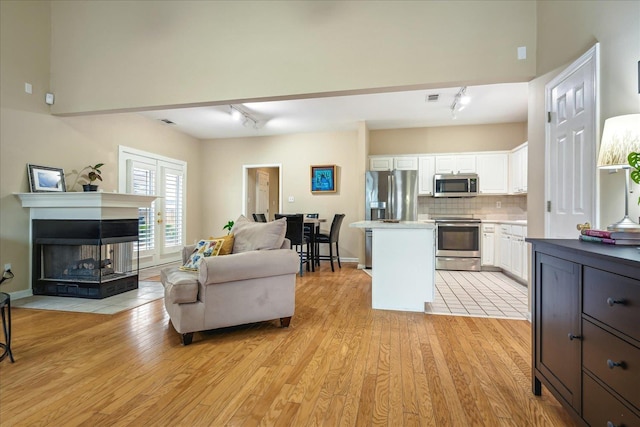 kitchen with white cabinets, a kitchen island, open floor plan, stainless steel appliances, and light wood-type flooring