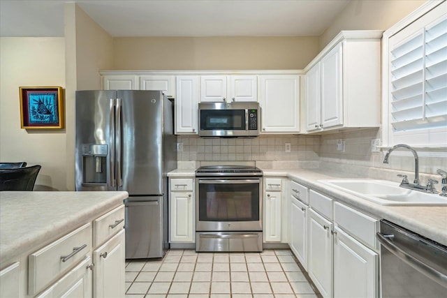 kitchen with stainless steel appliances, a sink, white cabinetry, light countertops, and tasteful backsplash