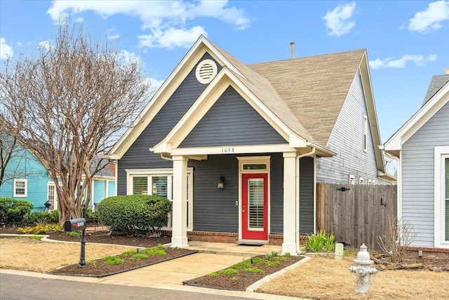 view of front of house featuring brick siding, roof with shingles, and fence