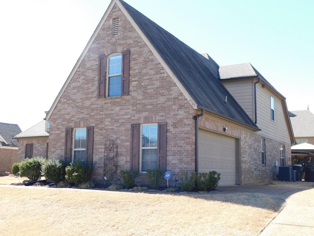 view of side of property featuring a garage, roof with shingles, central AC, and brick siding